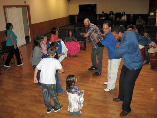 Guest teachers from Puerto Rico, Rafael Maya and Pablo Luis Rivera teach Bomba posture, figures, and steps to the children of the Bomba y Plena Workshop. In this picture, they are dancing alongside Workshop Co-director (center) Hector Lugo. Workshop Co-Director Shefali Shah is in the background next to the barrel drums, working with the children on percussion elements.